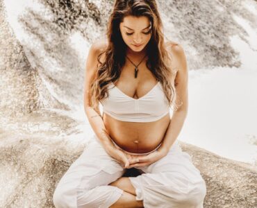 pregnant woman doing yoga with against the backdrop of a cascading waterfall