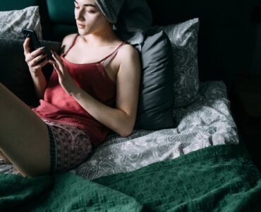 woman sitting on the bed while using her smartphone