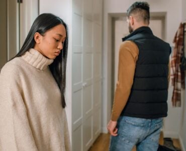a woman in cream sweater behind a person in black vest